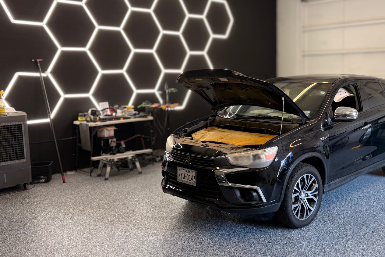 A black crossover with its hood open in the shop bay, under the hexagon LED ceiling