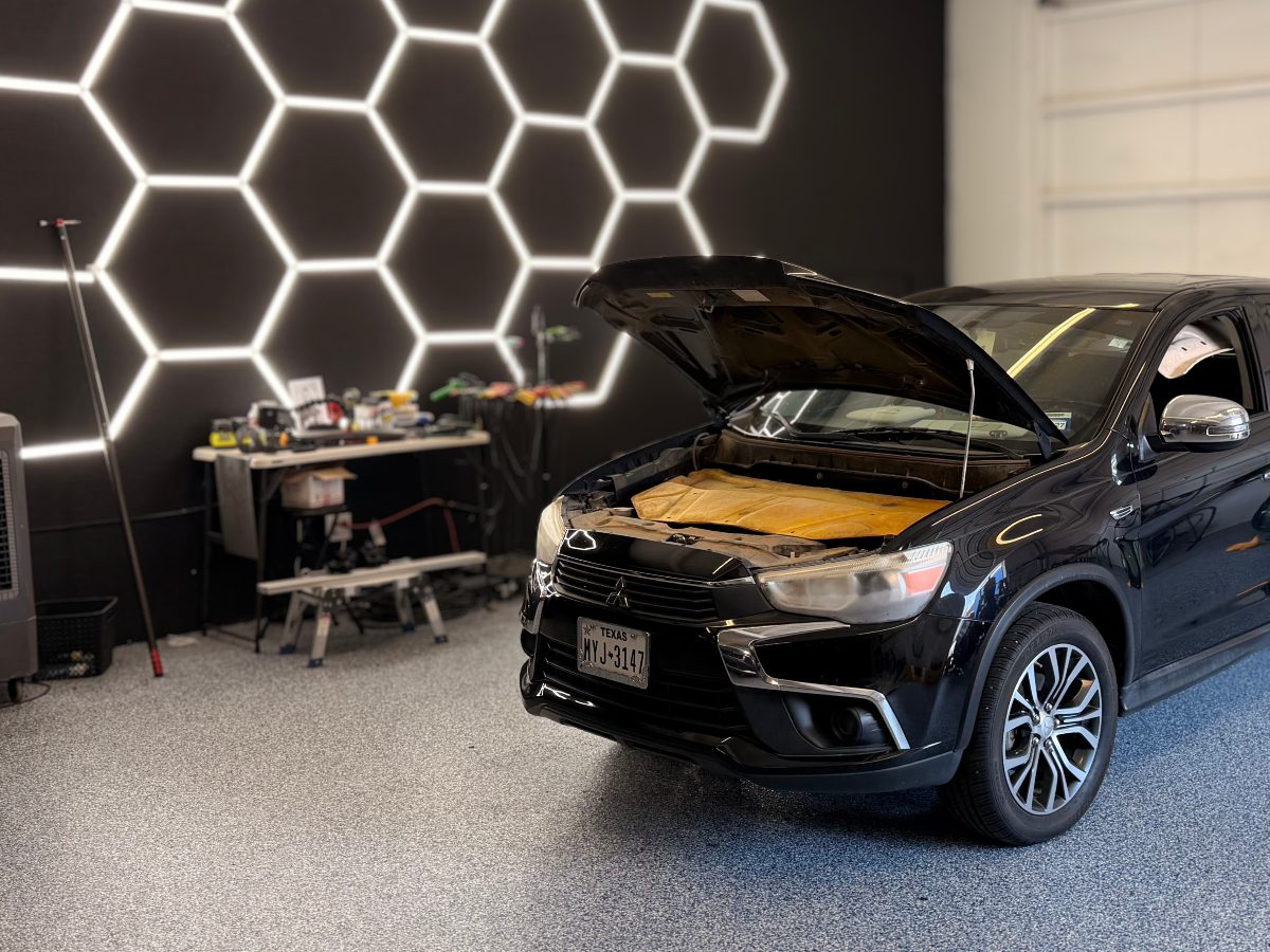 A black crossover with its hood open in the shop bay, under the hexagon LED ceiling