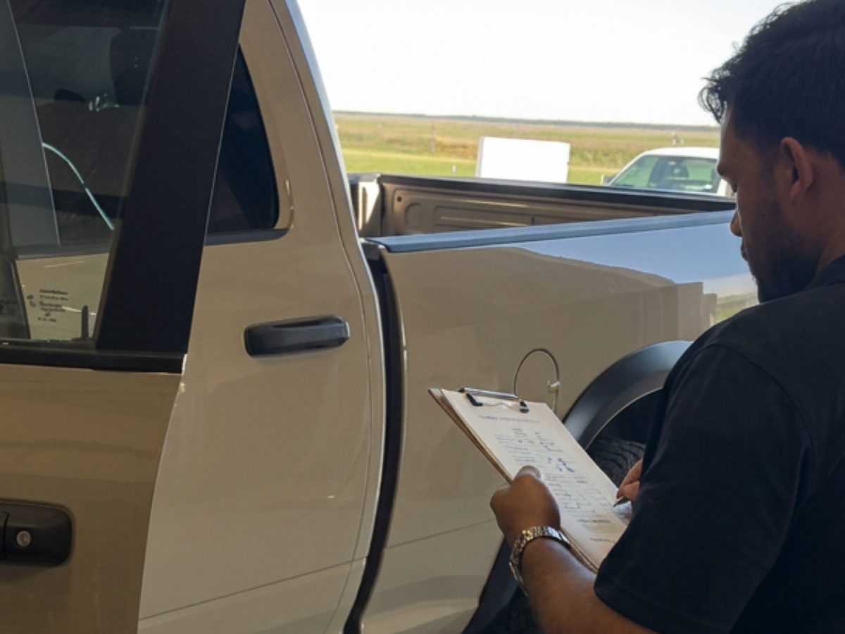 A technician with a clipboard walking around a tan pickup, writing down the damage