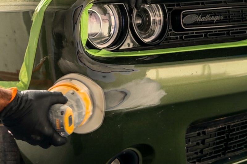 A gloved technician running a polisher across the front of a green muscle car