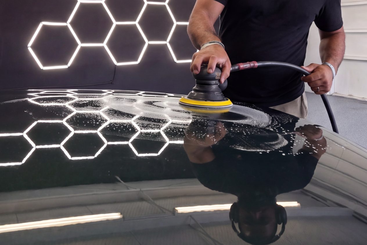 A polisher working compound across a black hood, the hexagon lights reflected in the paint