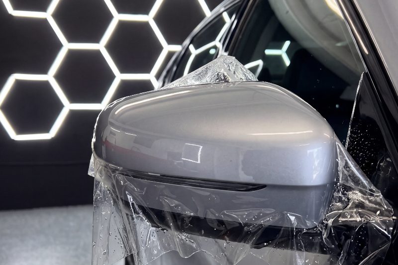 Protection film draped over a car mirror before it is worked down