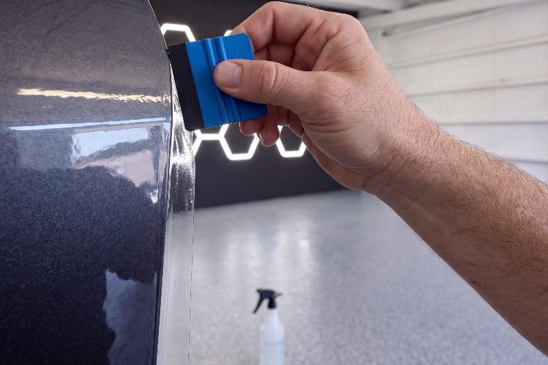 A blue squeegee pressing protection film along the edge of a dark door