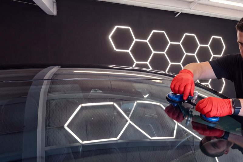 Gloved hands working a windshield with suction handles in the bay